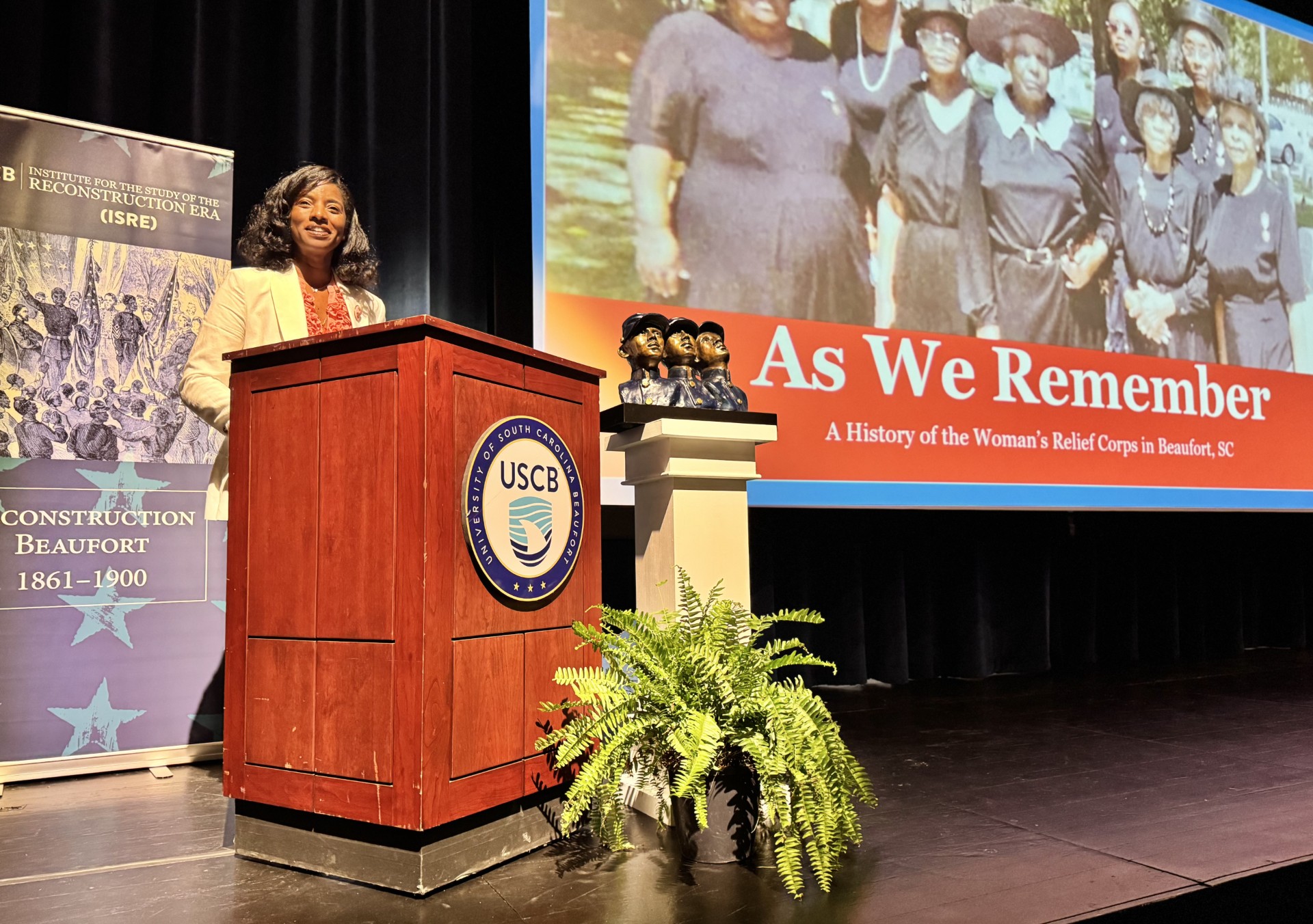 Dr. Najmah Thomas gives a presentation at a podium on a stage at the University of South Carolina, Beaufort