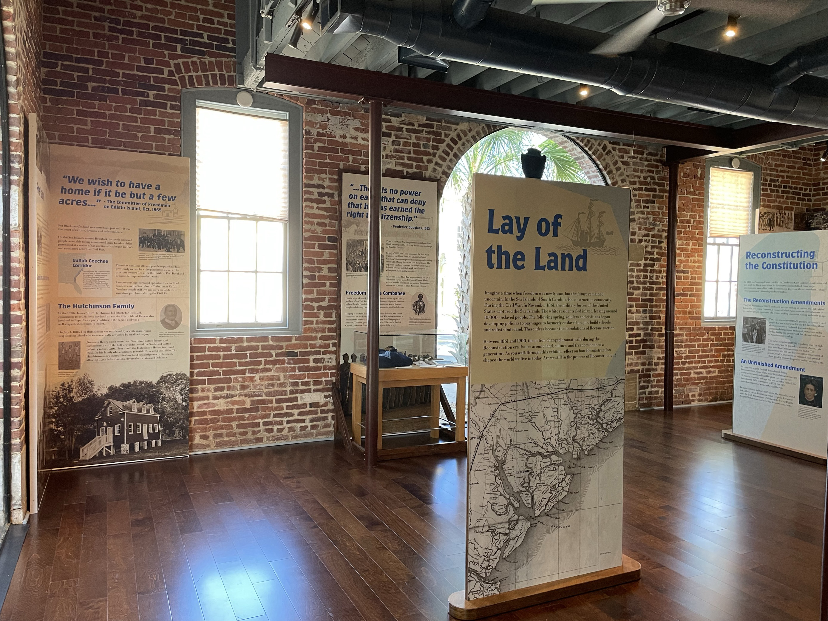 A series of upright exhibit panels in a room with wooden panels. Most prominent is a panel with a map of the coast of South Carolina with the title Lay of the Land