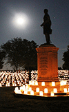 a darkened field with rows of luminaries and a Civil War monument