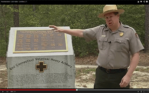 ranger next to tablet monument in wooded clearing
