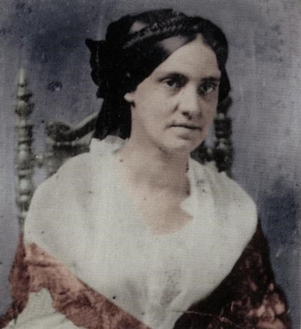 A color tinted photograph of a woman in 19th century clothing