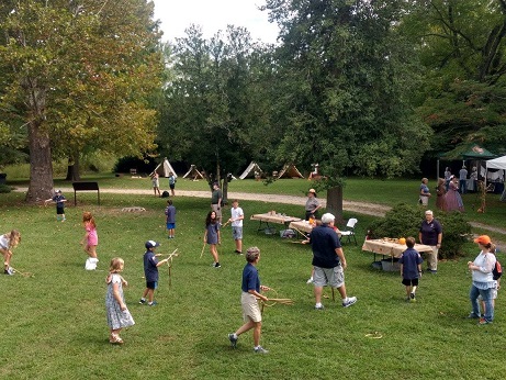 Children play historic games with sticks and hoops on a green lawn.