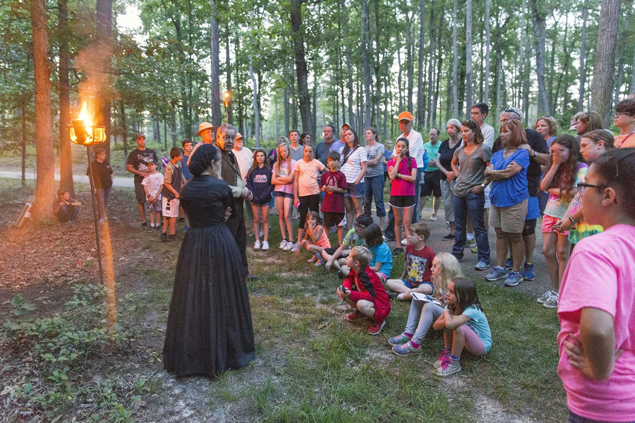 Living History at Cold Harbor A woman reenactor in 19-century clothing speaks to a crowd of people in the woods.