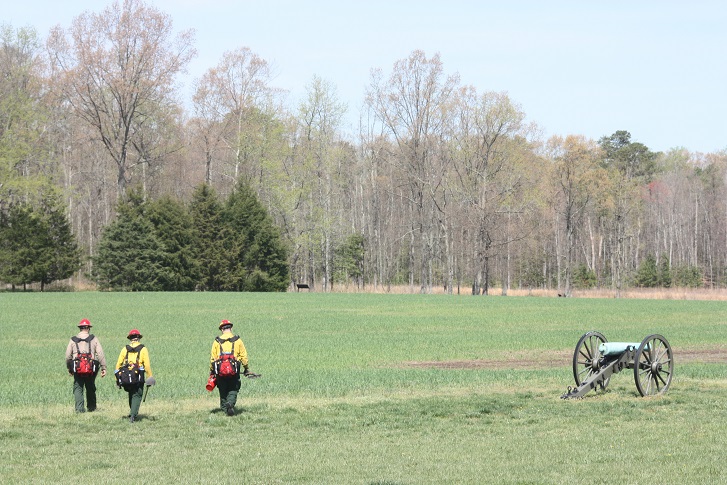 Three firefighters in a field beside a Civil War cannon.