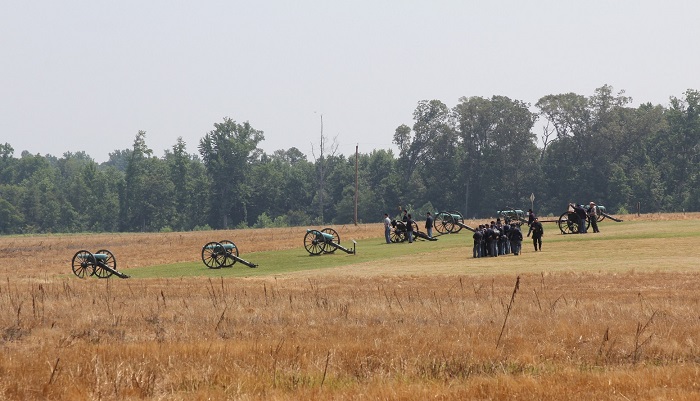 Civil War soldiers and a park ranger stand near 12 cannons