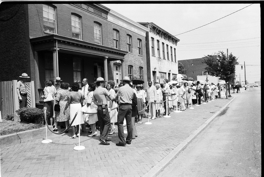Opening day of the Maggie L. Walker National Historic Site - 1985 A black and white photo of park rangers and a line of visitors on a city street.