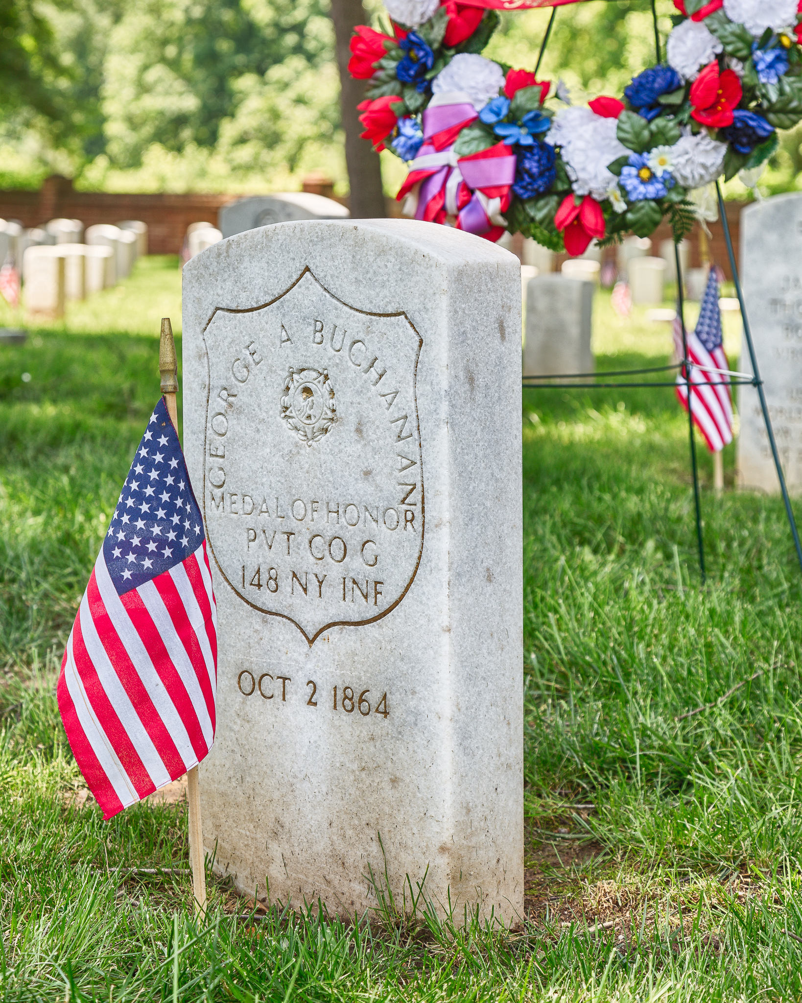 A U.S. soldier's tombstone, dated 1864, with a small American flag beside it.