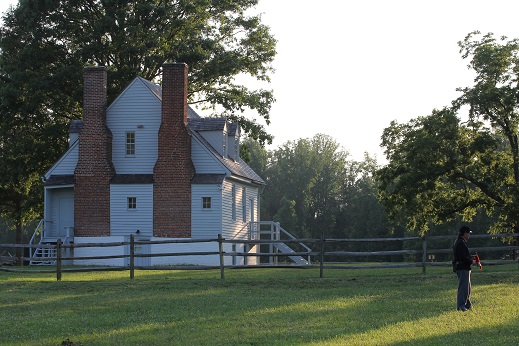 A single Civil War solider with a bugle stands beside an historic home.