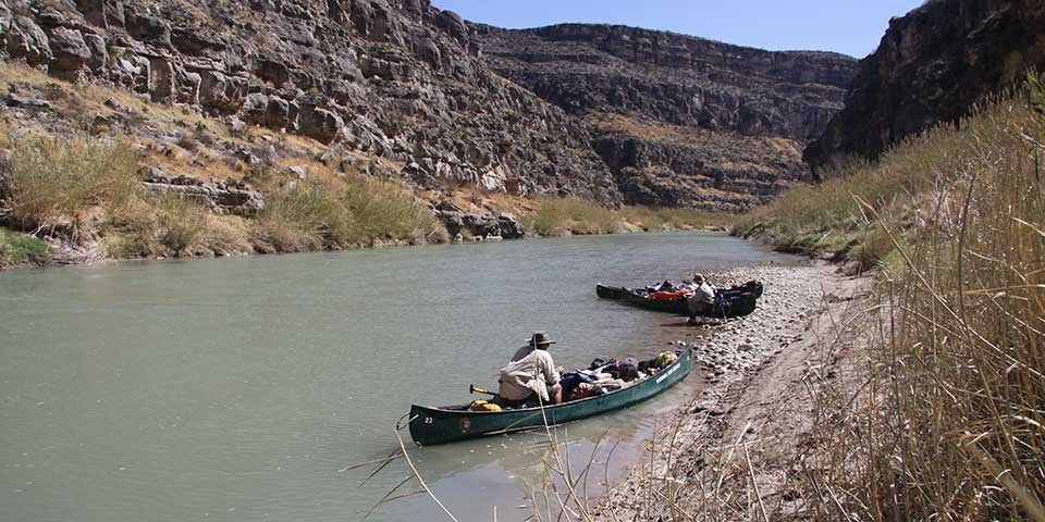 Scientists bank their canoes on a beach in a desert river canyon.
