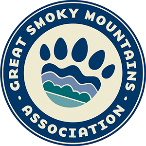 A circular logo with a multicolored bear paw in the middle and tan text circling the paw that says, "Great Smoky Mountains Association".