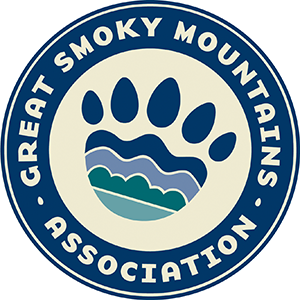 GSMA Logo A circular logo with a multicolored bear paw in the middle and tan text circling the paw that says, "Great Smoky Mountains Association".