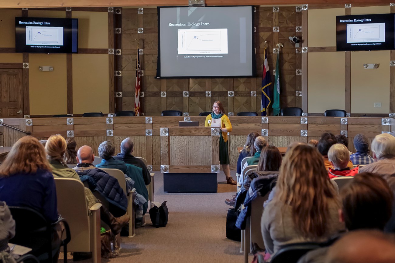 A woman stands at a podium in front of an audience