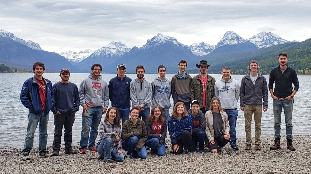 A group of students stand in front of lake with mountains in the background.