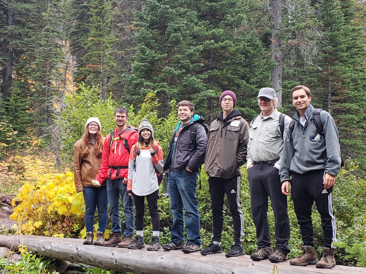 Professor Fred Bianchi stands on a log with a group of students.