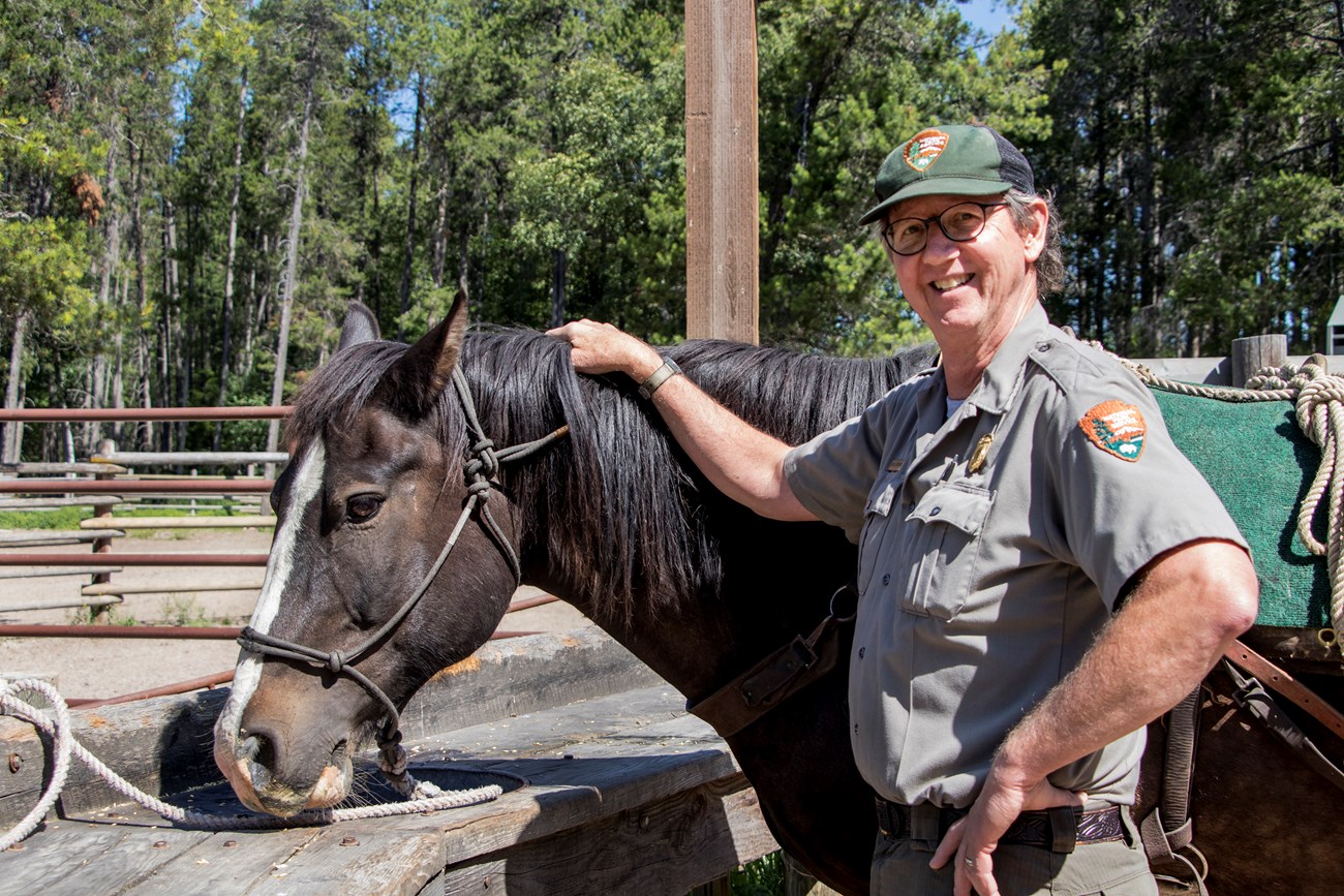 Ranger stands next to a horse, smiling for the camera.