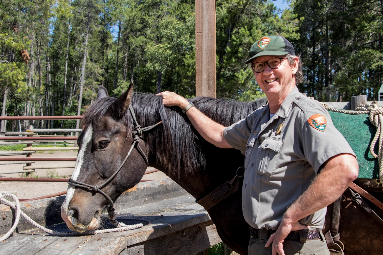 Ranger Chuck Cameron and horse Siyeh Ranger stands next to a horse, smiling for the camera.