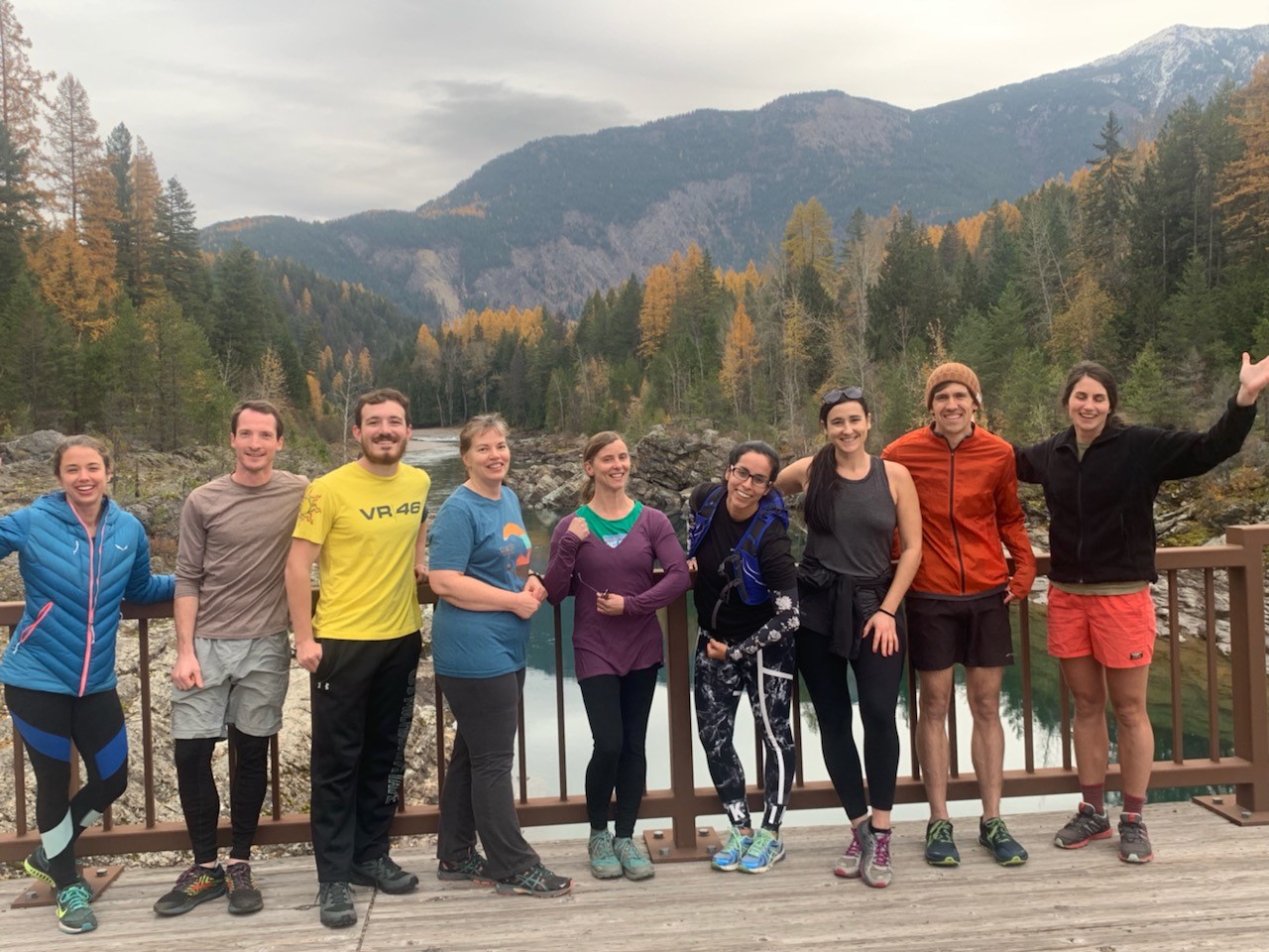 A smiling group of people stands on a bridge in front of a forested background
