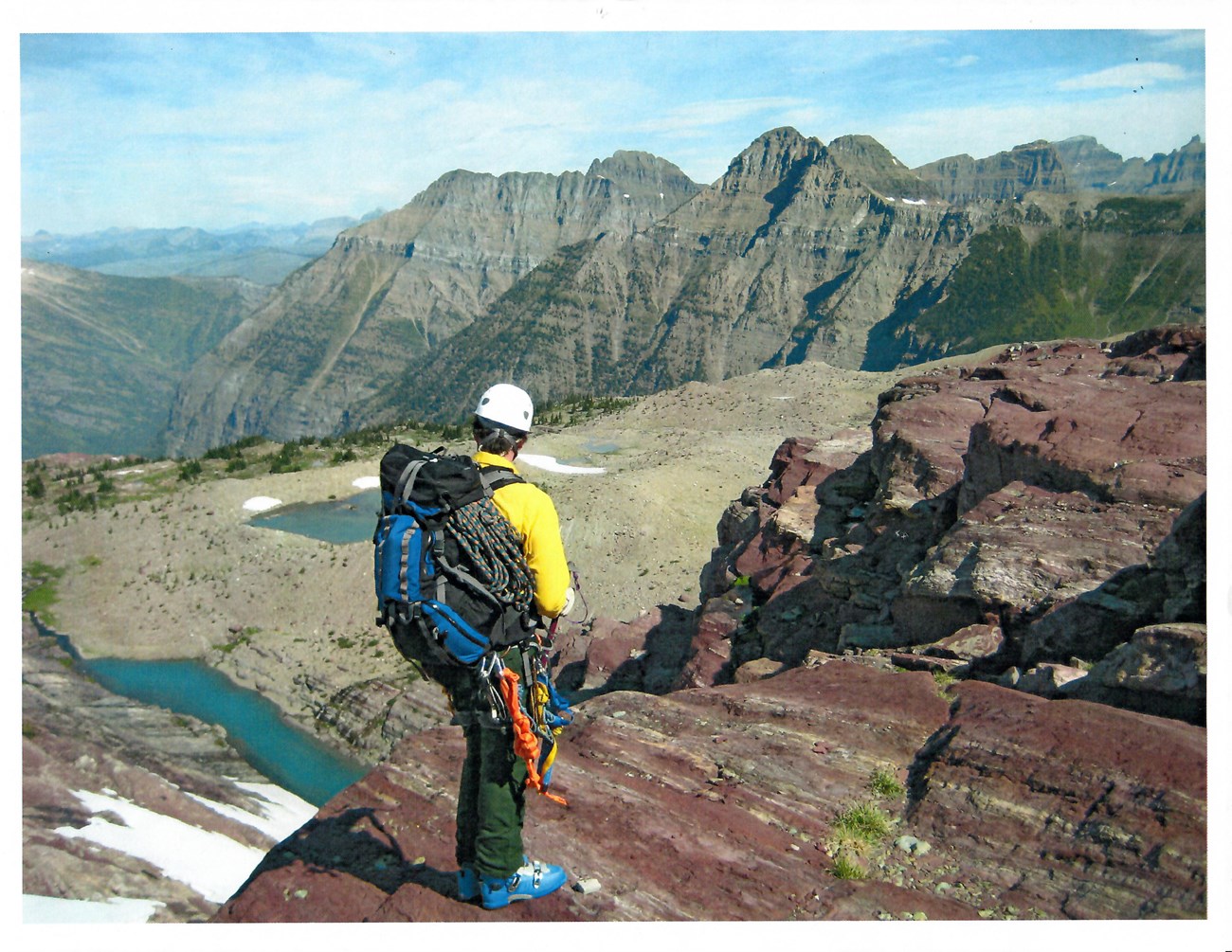 Man with backpack and ropes stands on a rock ledge.