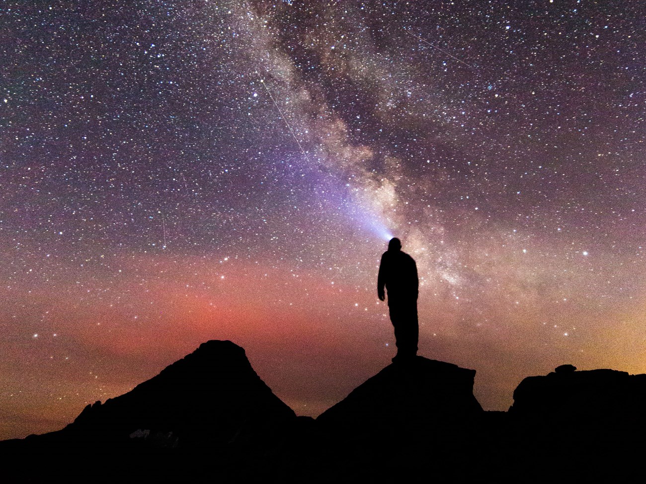 A hiker looking up at the Milky Way A hiker standing on rocks is silhouetted in black while looking up at the Milky Way at night