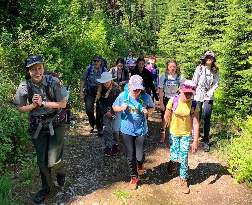 Students hike with park ranger A group of girls hike with park rangers up a wooded trail.