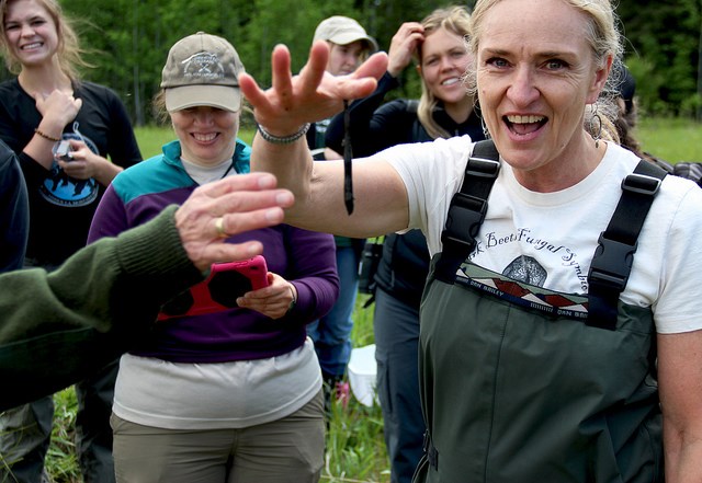 Dr. Diana Six shows a leech to students. A leech dangles from Dr. Diana Six hand as students stand in amazement behind her.