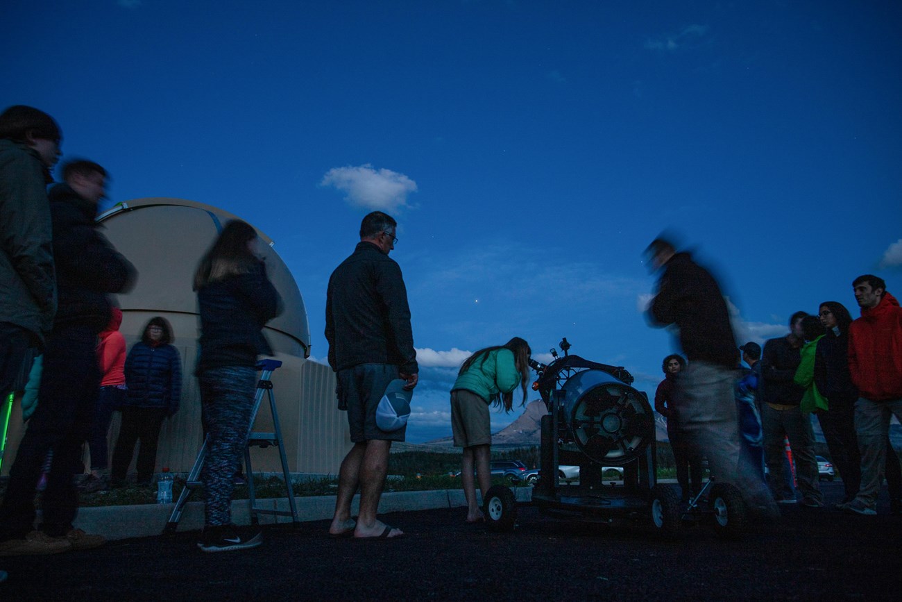 A group of people look through telescopes at twilight