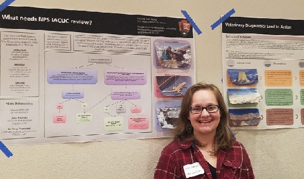 A woman stands in front of two NPS posters taped to the wall. They describe the NPS Wildlife Health Branch services.