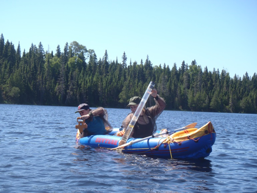 Water Sampling on Isle Royale Two field technicians lower instruments over the edge of an inflatable boat and into the water.