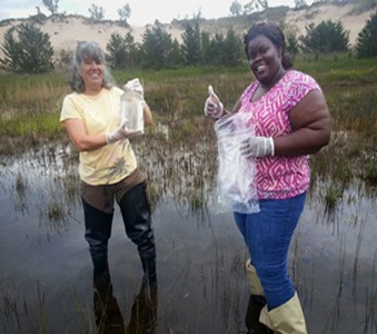 Two women standing in a wetland prepare to collect water samples.