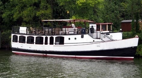 The Emita II awaits educators attending the September 22nd floating workshop. A tour boat is docked along the edge of a Great Lakes Tributary. The water is in the foreground, and the forested shoreline is visible behind the boat.
