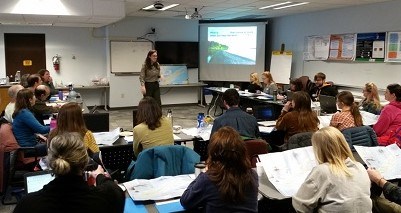 Teachers learned about Isle Royale National Park and tried activities they could use with their students. A woman wearing an NPS uniform stands before a group seated at tables. A projection screen is in the background.