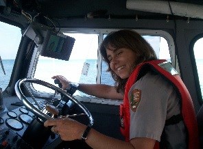 A woman inside the cab of a boat smiles as she steers.