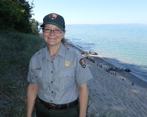 A woman in a National Park Service uniform stands high above the sandy shoreline of Lake Michigan.