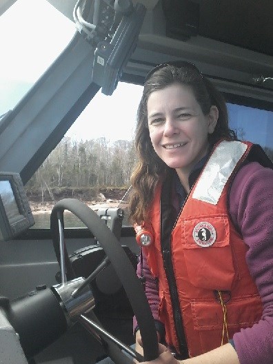 A woman inside the cab of a boat smiles as she steers.