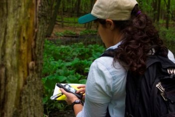 A young woman at a vernal pool works with a GPS unit.
