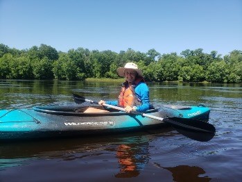Intern Olivia Poelmann monitoring for invasive yellow irises. A woman in a blue kayak floats down a river.