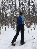 Early snows on the island bring opportunities to ski out to research locations in the wilderness. A woman cross country skis down a forest trail.