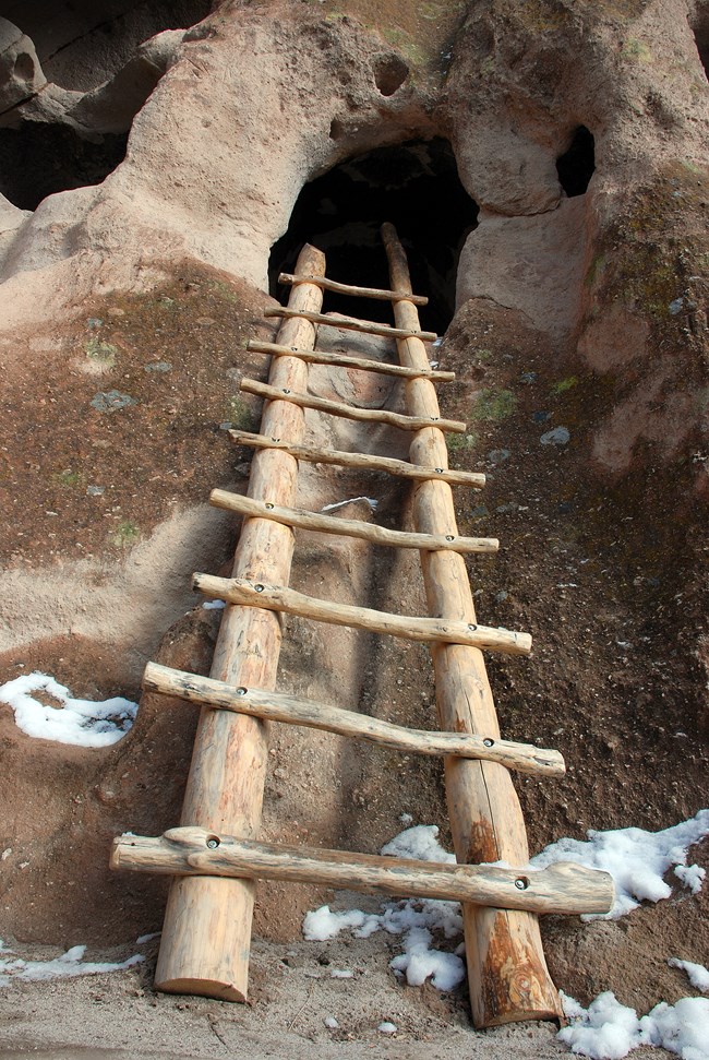 A wooden ladder leads into a small cavity in a rock wall