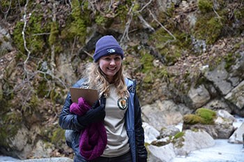 an intern stands holding a clipboard and smiling