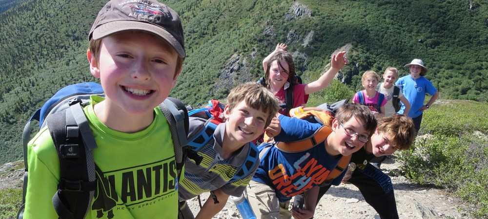 A group of kids smile while hiking up a hill