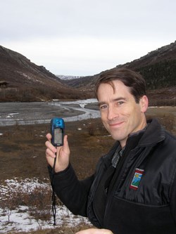 man holding a small electronic device, a river and hills in the background man holding a small electronic device, a river and hills in the background