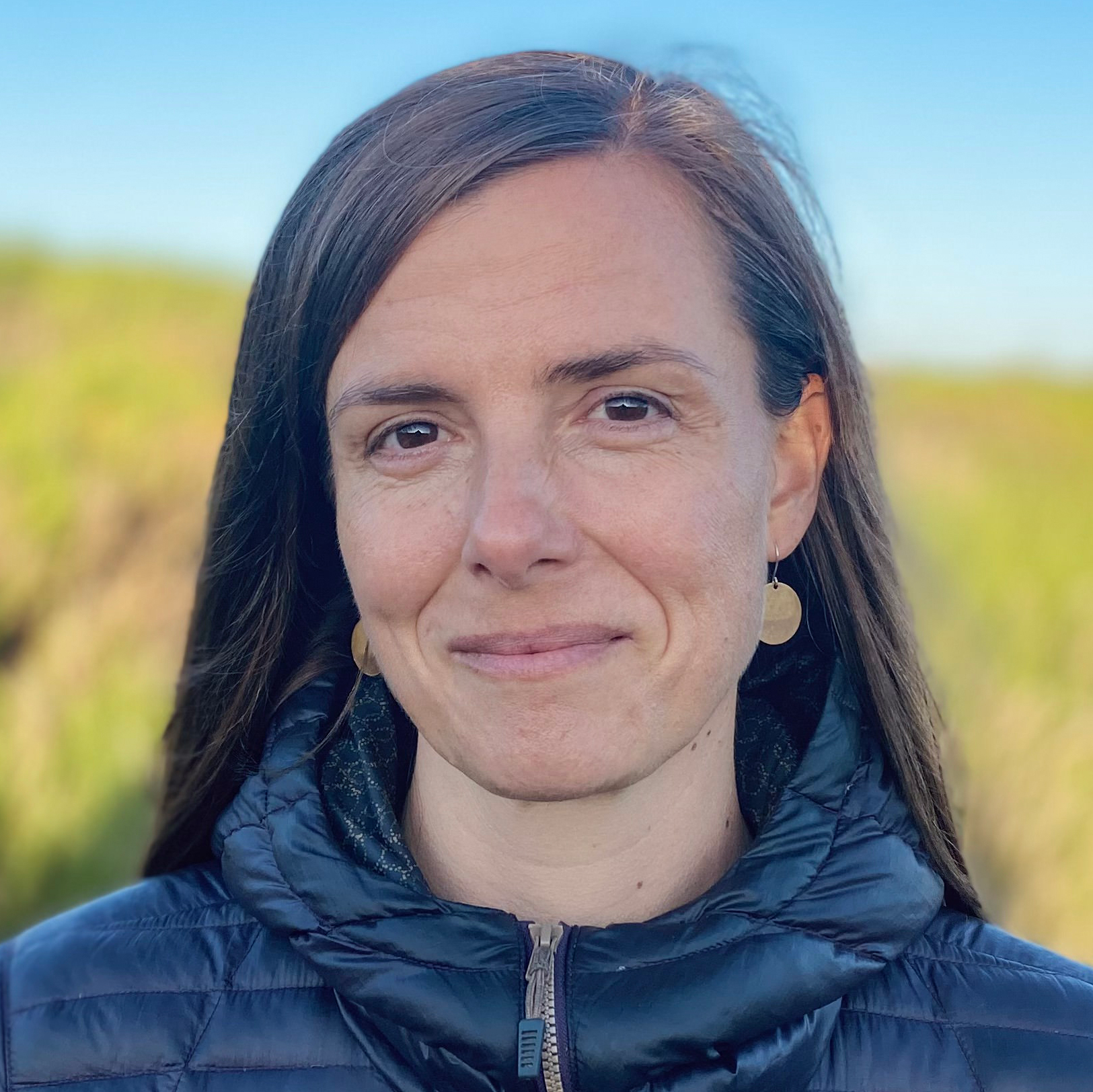 Headshot of Meade Krosby, a smiling white woman with long brown hair outdoors.