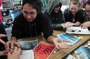 Four students inspect small items and photos in a classroom.