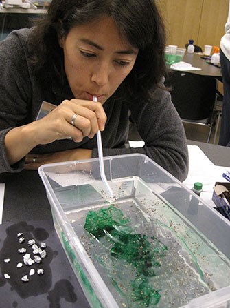 Oil spill simulation A woman blows through a straw into a tub filled with water