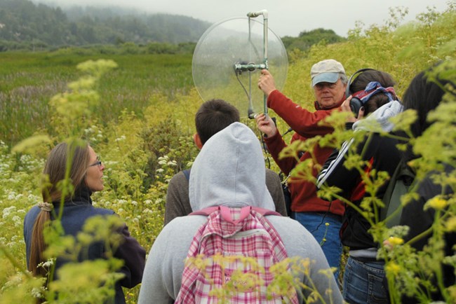 Students join an expert studying bird calls with a special, targeted listening device