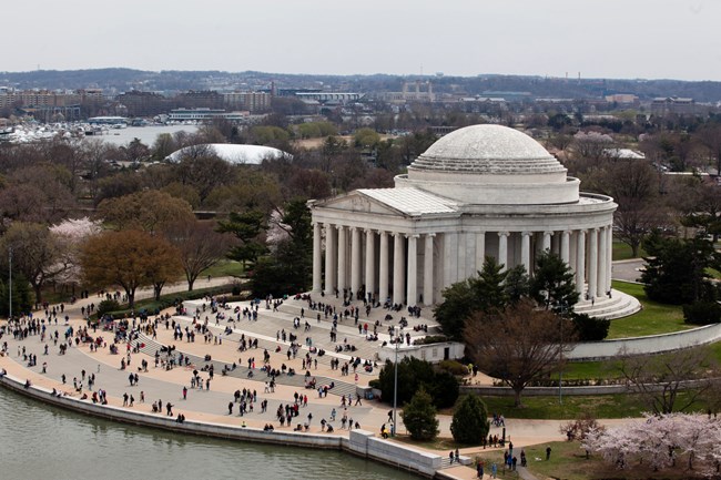 An aerial view of the Thomas Jefferson Memorial with several visitors walking up the steps. Memorial dome has blackened rings around it.