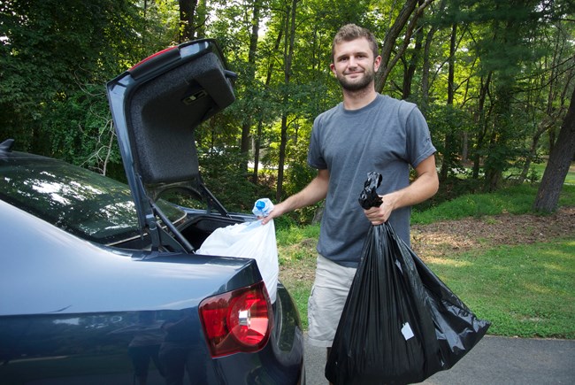 Person holding bag of trash near open car trunk