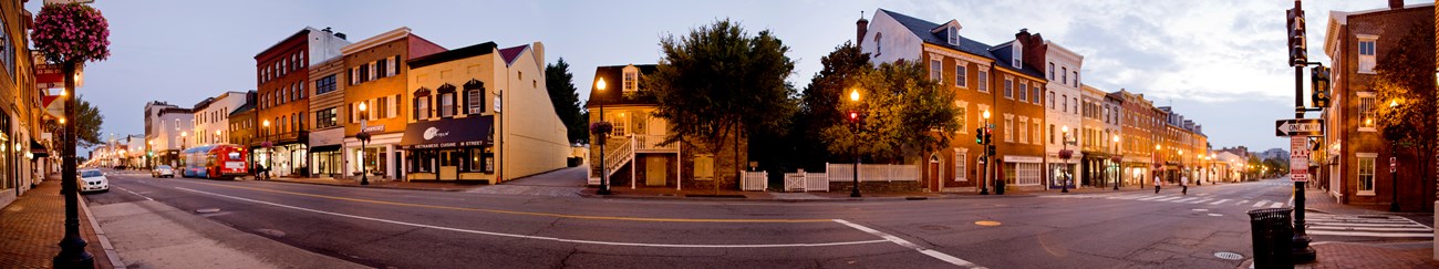 A panoramic view of a stone house in the twilight illuminated by city street lamps