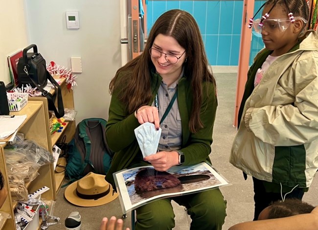 A park ranger holds a beaver hind print in a classroom for students to see and feel