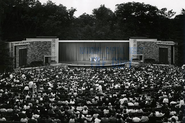 A crowd sits in the amphitheater waiting for a performance to begin.